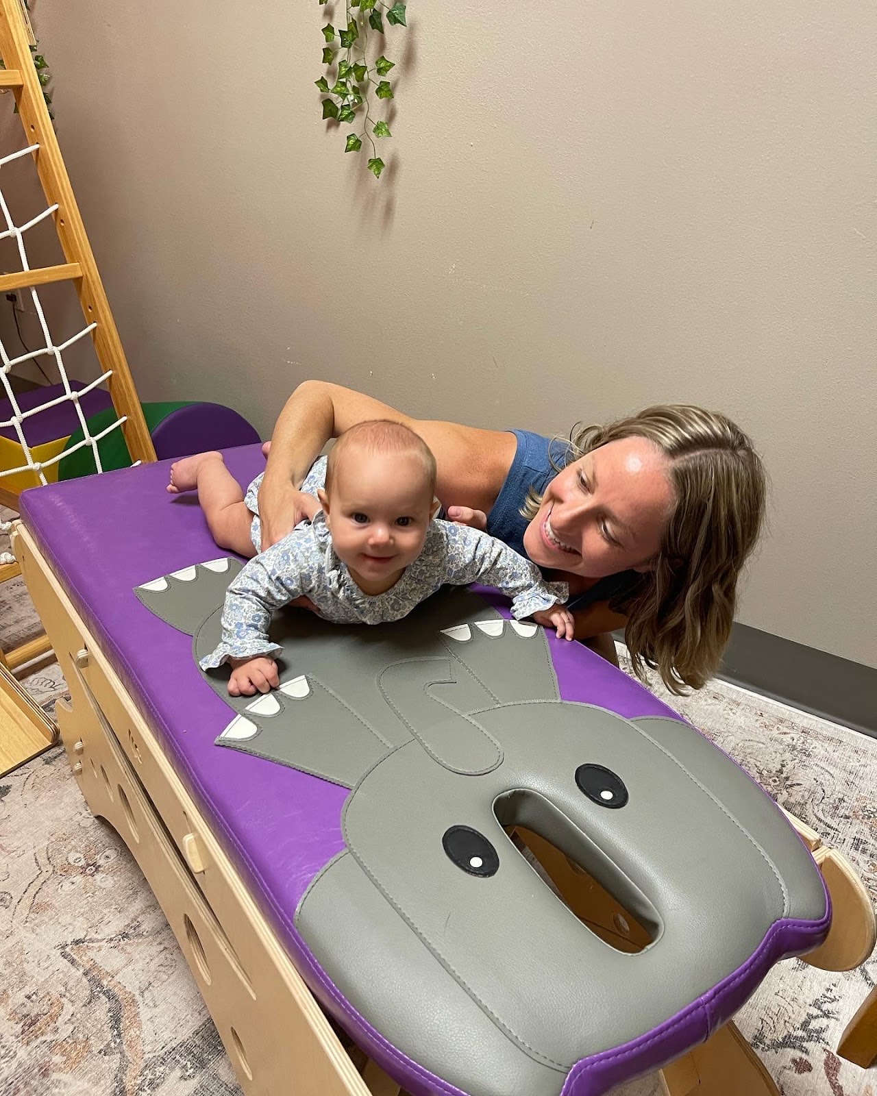 A smiling baby on the playful elephant-themed pediatric table in the Little Roots wing while a practitioner provides gentle care