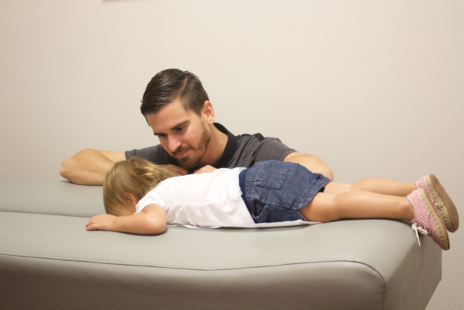 A father resting beside his toddler on the adjustment table, sharing a calm moment of care